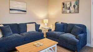 A living room with two blue sofas, a wooden coffee table, and a small side table with a lamp.