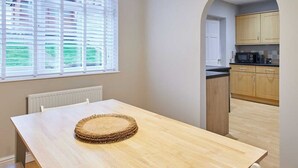 A dining area with a wooden table, three pendant lights, and a view of the kitchen through an archway.