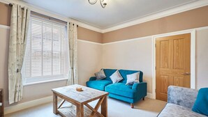 A living room with a blue sofa, a grey sofa, a wooden coffee table, a window with curtains, and a wooden door. - Host Stay Oliver s Den (Alnwick)