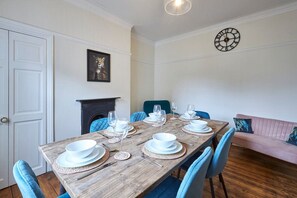 A dining room with a wooden table set for six, blue chairs, a fireplace, a clock, and a pink sofa. - Host Stay Oliver s Den (Alnwick)