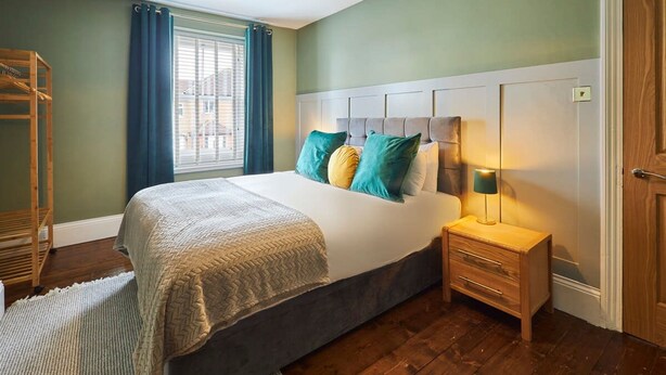 A bedroom with a bed, bedside table, lamp, and a window with curtains. - Host Stay Oliver s Den (Alnwick)