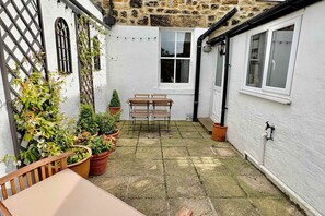 A courtyard with a wooden table and chairs, potted plants, a stone wall, and a window. - Host Stay Oliver s Den (Alnwick)