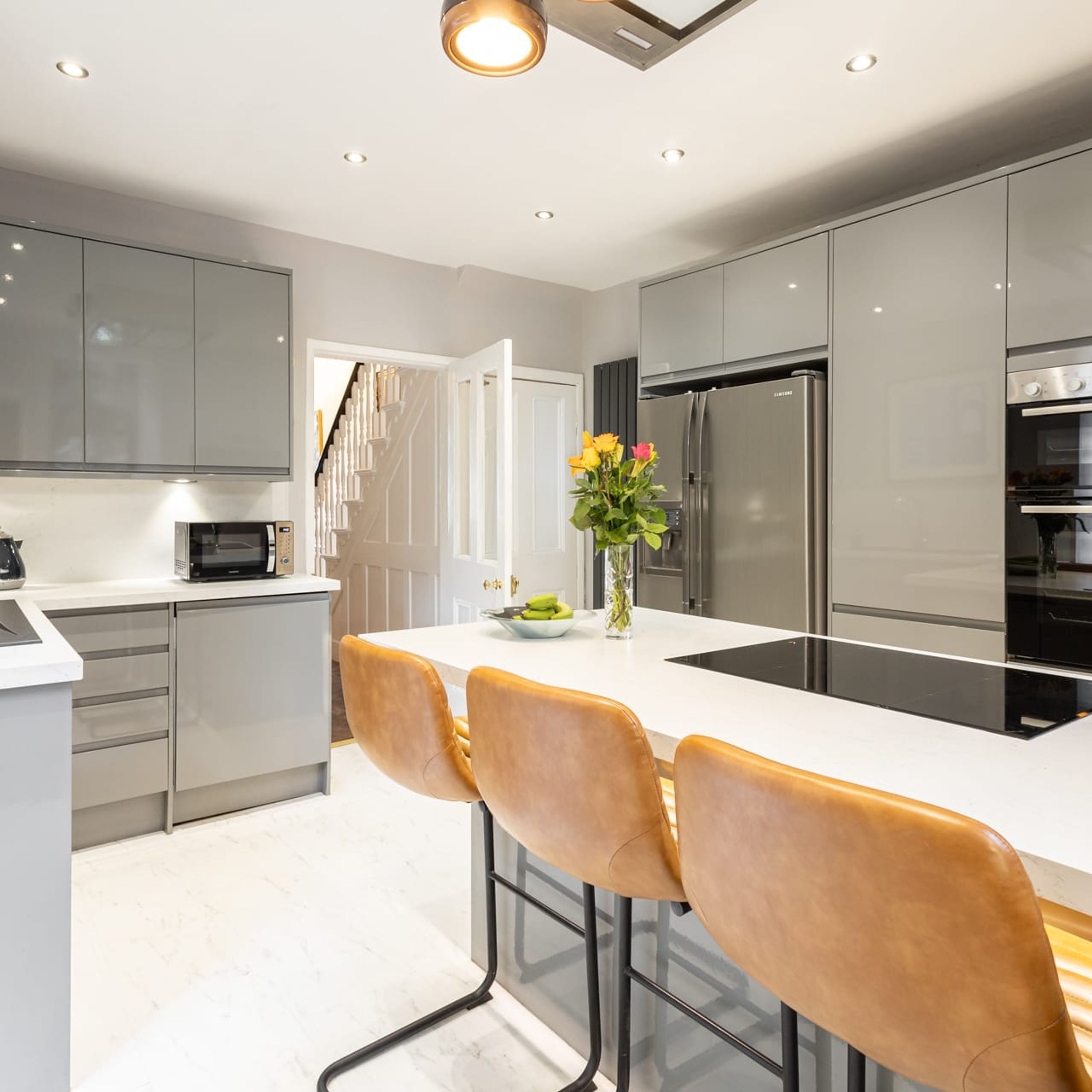 A modern kitchen with stainless steel appliances, a white countertop, and a bar area with leather chairs.