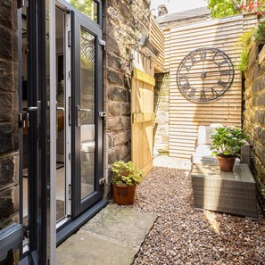A small courtyard with a wooden fence, a stone wall, a large clock, and potted plants. - Host Stay Rock End (Matlock)