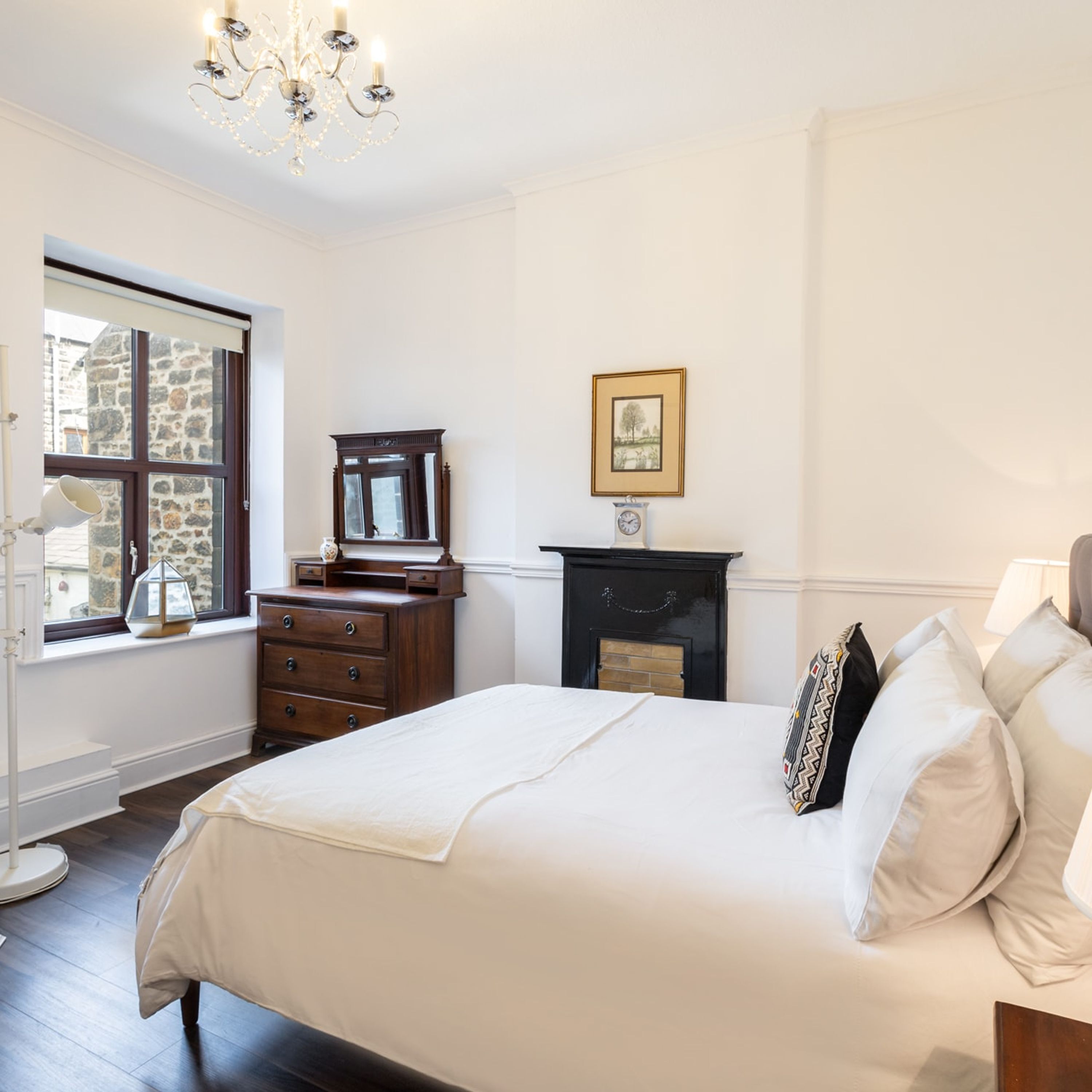 Une chambre à coucher avec un grand lit, une commode, un miroir, une horloge et un tableau encadré accroché au mur.