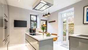 A modern kitchen with a central island, built-in appliances, and a flat-screen TV. - Host Stay Rock End (Matlock)