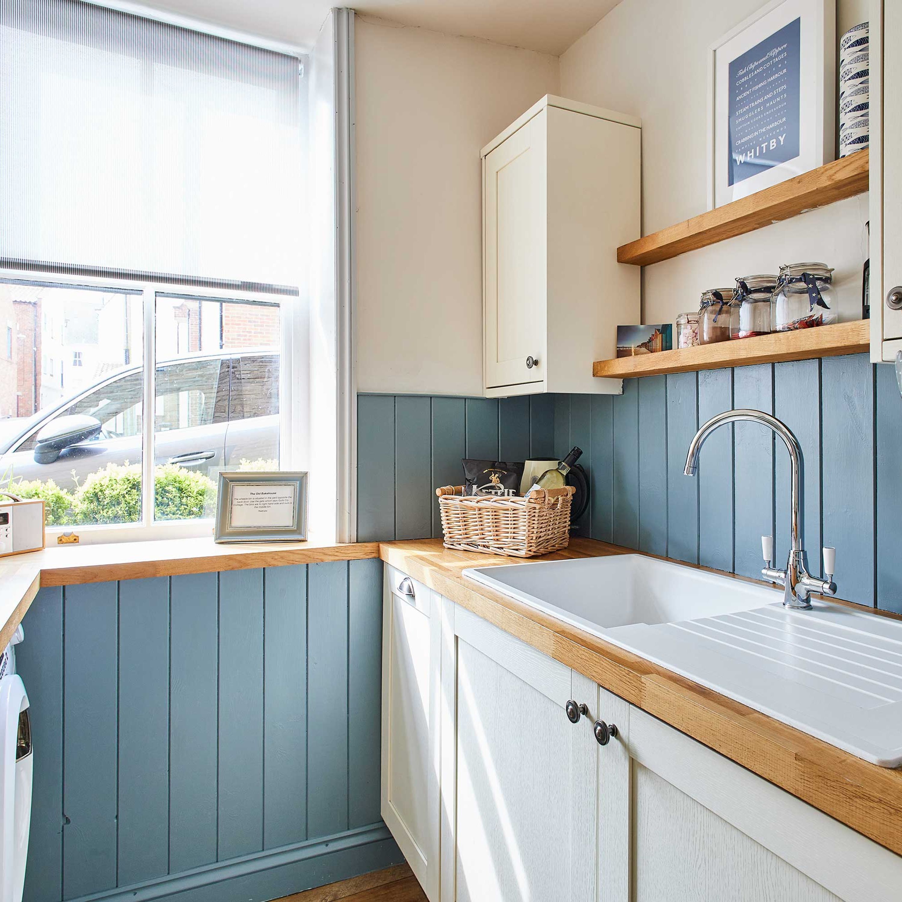 A kitchen with a window, a sink, a cabinet, and a shelf with jars.