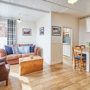 A cozy living room with a brown leather sofa, a wooden coffee table, and a dining area with a wooden table and chairs. - Host Stay The Old Bakehouse (Whitby)
