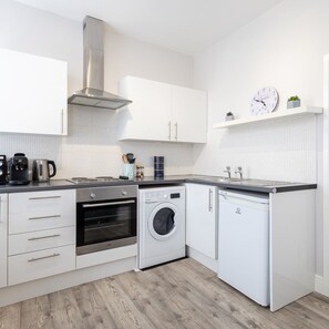 A modern kitchen with white cabinetry, a stainless steel range hood, a built-in oven, a dishwasher, and a washing machine. - Host Stay North Sands Rest (Scarborough)