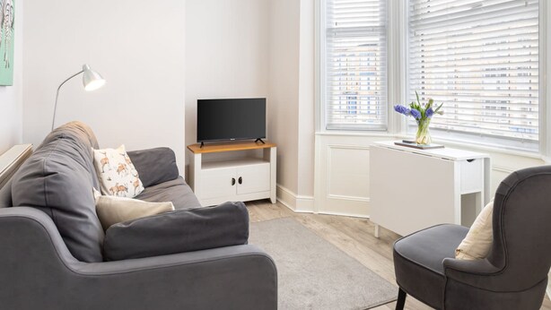 A modern living room with a grey sofa, a small white desk, and a TV on a wooden stand. - Host Stay North Sands Rest (Scarborough)