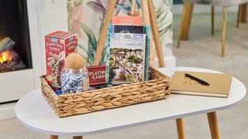 A table with a woven basket containing a box labeled "Tumbling Tower," a bottle of honey, a box of playing cards, and a notebook with a pen.