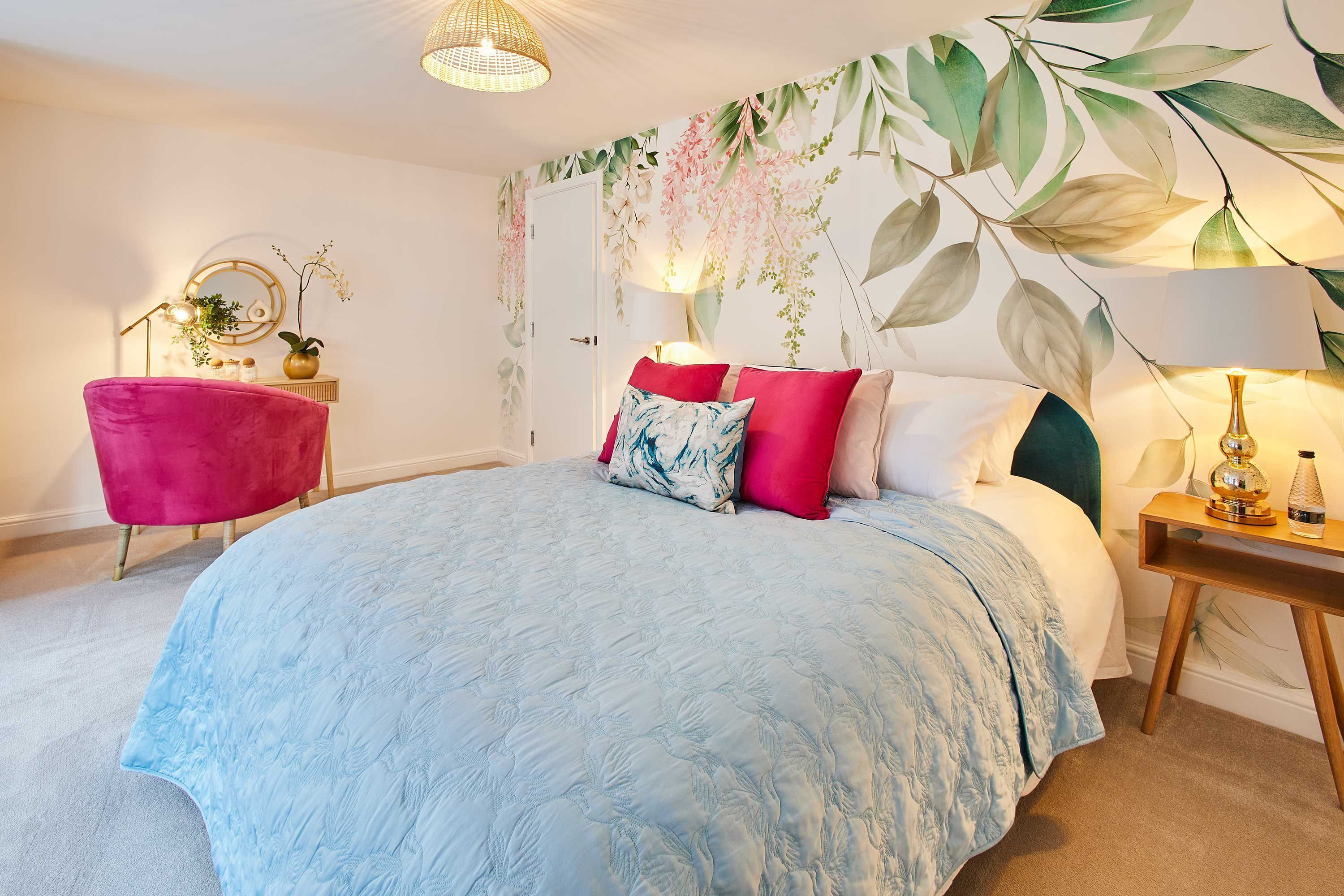 A bedroom with a large bed, a desk, a chair, and a wall with a leafy pattern.