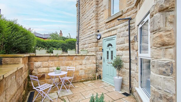 A stone building with a small patio area featuring a table and chairs, a door, and a window. - Host Stay Apartment 1 Dane Court (Harrogate)