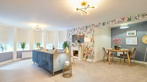 A modern reception area with a sofa, a round table, and chairs. There is a decorative lamp, a small plant, and a wall-mounted TV. - Host Stay Apartment 1 Dane Court (Harrogate)