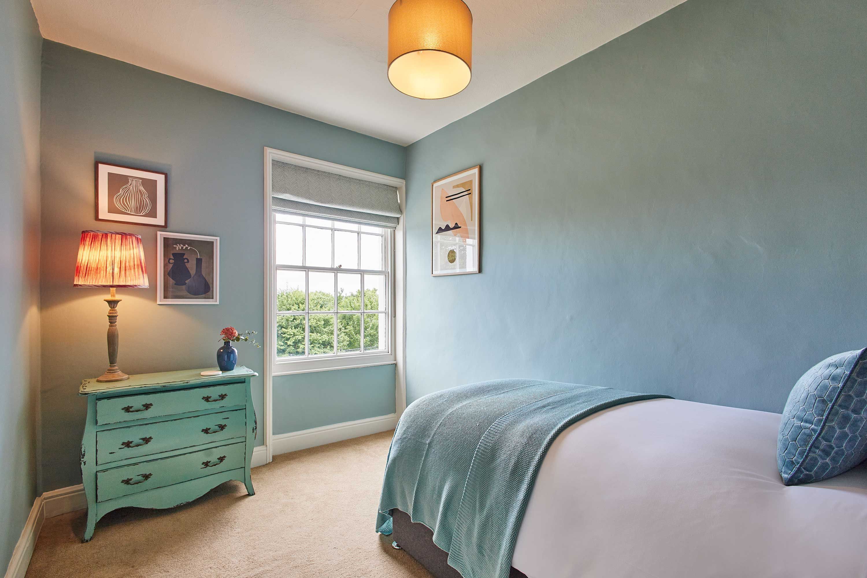 Une chambre à coucher avec un lit, une commode, une fenêtre et des œuvres d’art murales.