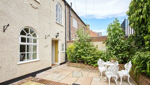 A patio with white chairs and a table, a brick wall, and a window with a white frame.
