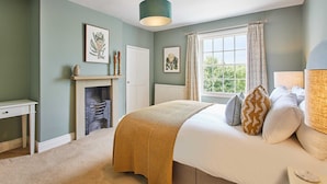 A bedroom with a bed, a fireplace, a window with curtains, and a ceiling light.
