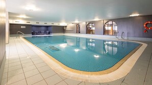 Ein großes Hallenbad mit klarem, blauem Wasser, gefliestem Boden und einem Rettungsring an der Wand.