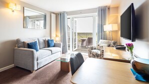 Ein Hotelzimmer mit grauem Sofa, einem Couchtisch, einem Fernseher und einem Balkon mit Blick.