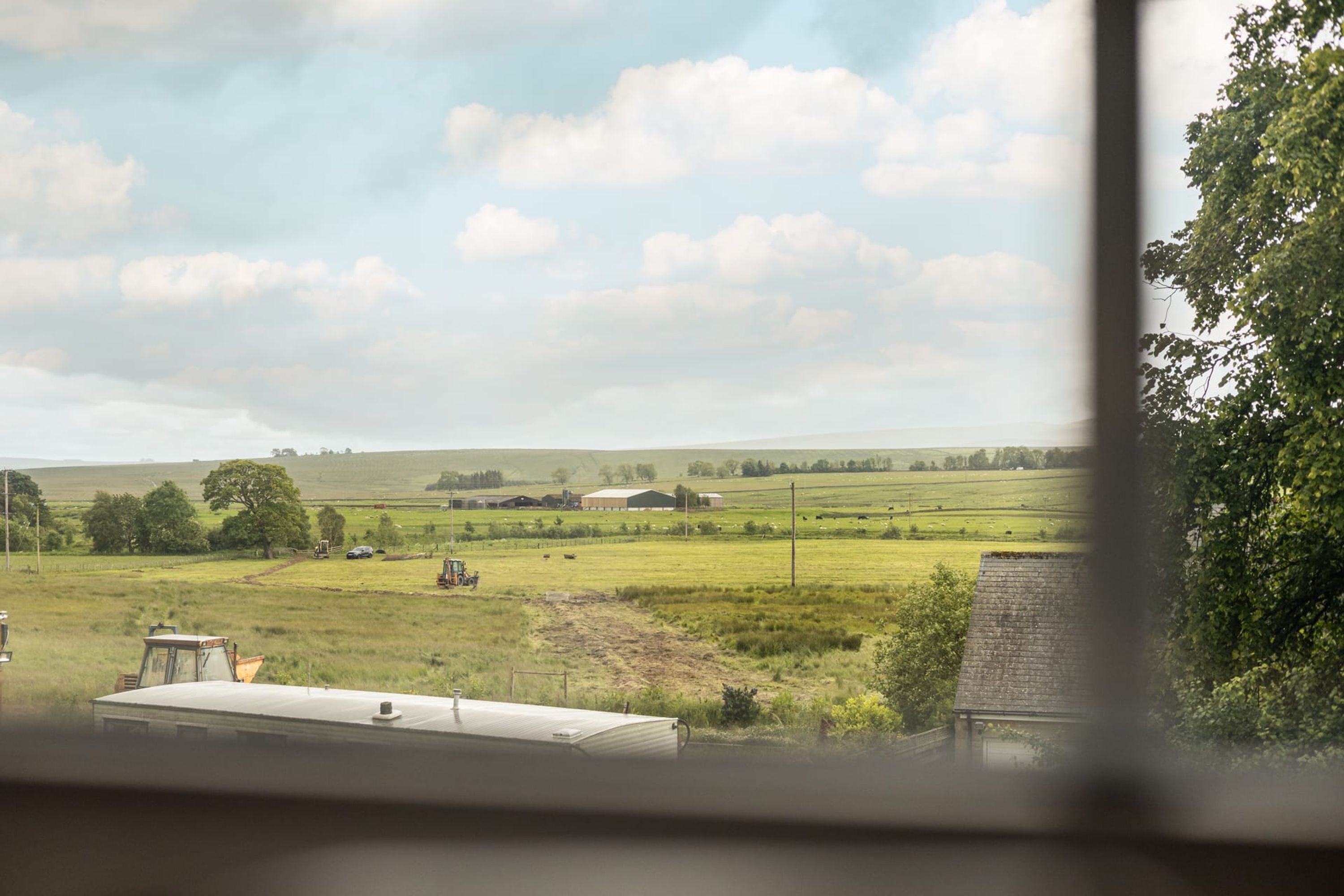 A rural landscape with fields, a tractor, and farm buildings.