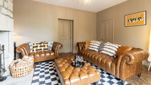 A living room with two leather sofas, a patterned rug, a chandelier, and a fireplace. - Host Stay Bankfoot Cottage (Newcastle-upon-Tyne)