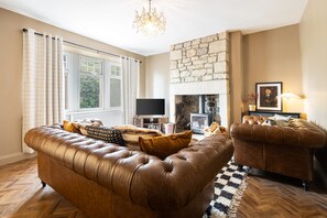 A living room with a stone fireplace, leather sofas, a television, and a chandelier. - Host Stay Bankfoot Cottage (Newcastle-upon-Tyne)