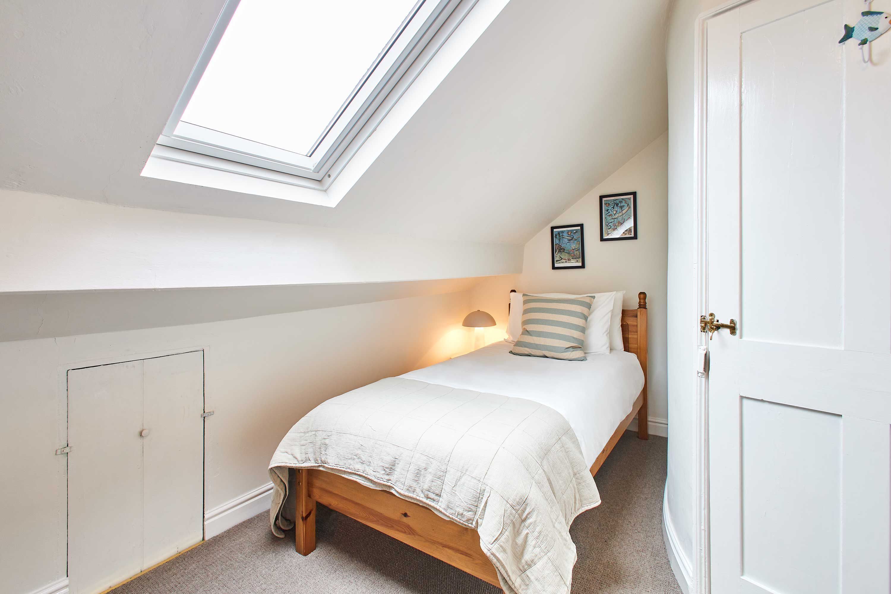 A bedroom with a skylight, a bed with a white duvet, a bedside lamp, and a door with a brass handle.
