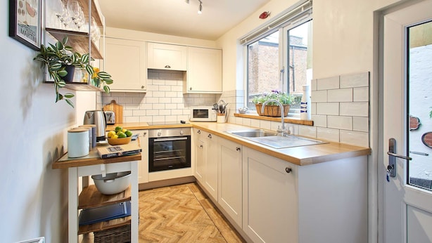 A compact kitchen with white cabinets, a wooden countertop, and a window providing natural light. - Host Stay Sunstar (Whitby)