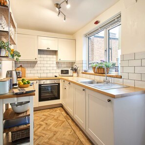 A modern kitchen with white cabinets, a wooden countertop, a built-in oven, a microwave, and a window with a view of a brick building. - Host Stay Sunstar (Whitby)