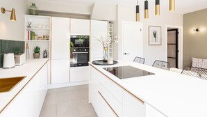 A modern kitchen with white cabinetry, a central island, and a dining area with a black metal chair. - Host Stay The School House (Hereford)