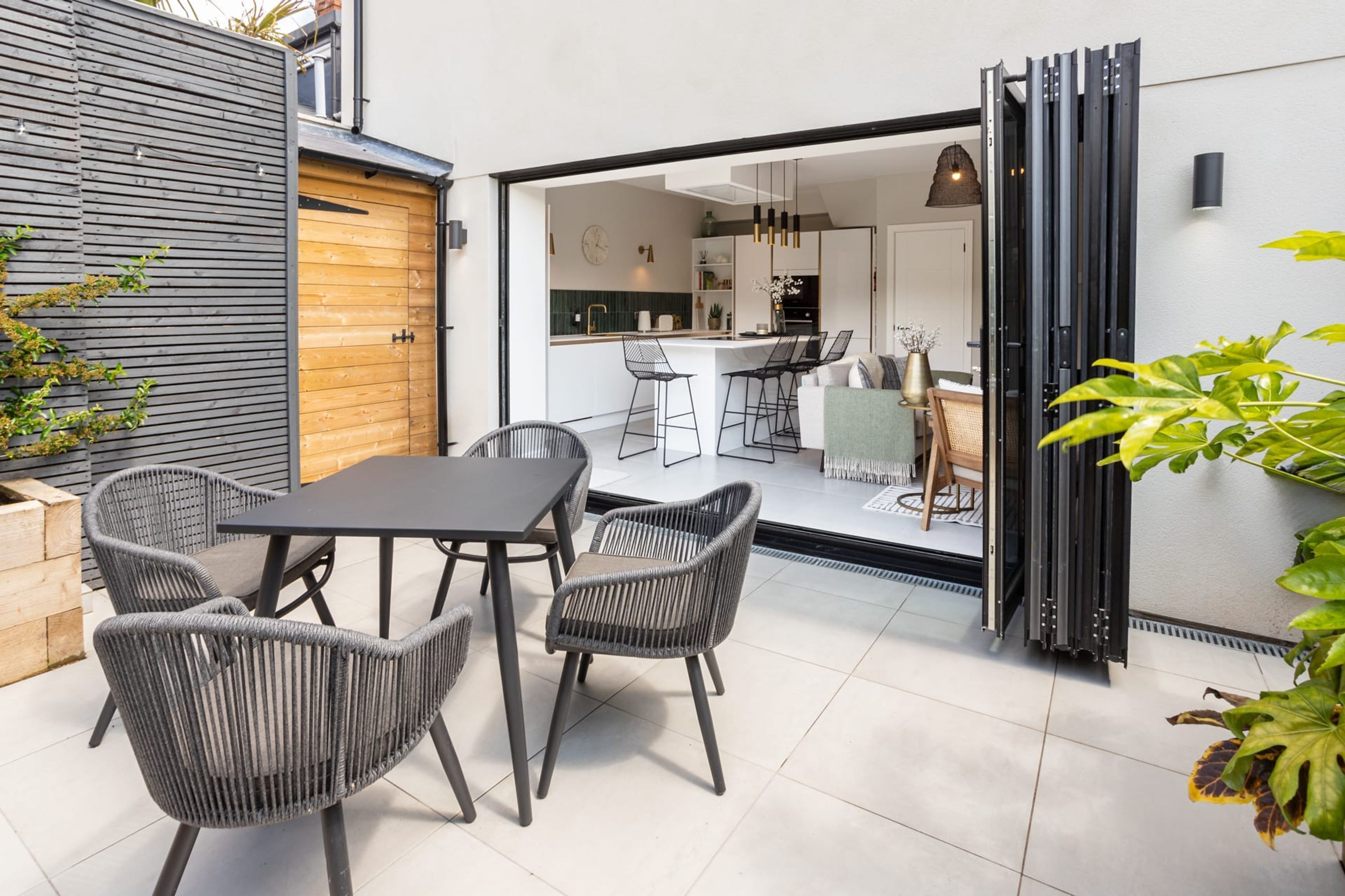 Une terrasse moderne avec une table et des chaises, une porte en bois et une vue sur la cuisine et le salon.