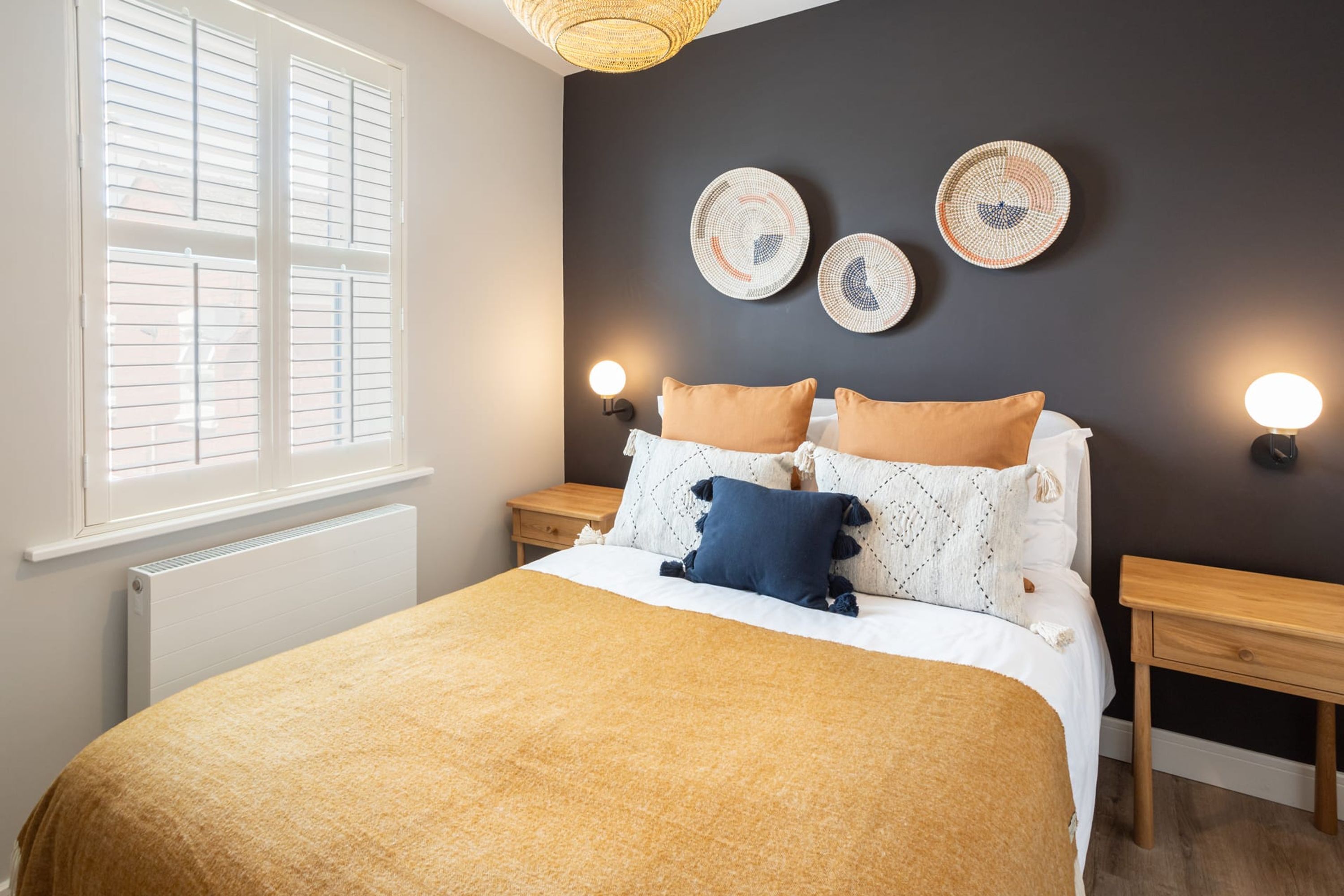 A bedroom with a bed, bedside tables, wall-mounted lights, and a window with blinds.