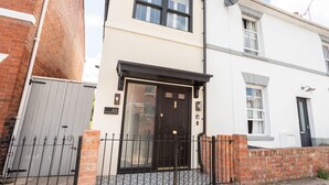 A two-story residential building with a black front door, a brick wall, and a metal gate. - Host Stay The School House (Hereford)