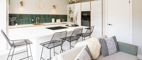 A modern kitchen with a central island, bar stools, and a sofa with cushions.