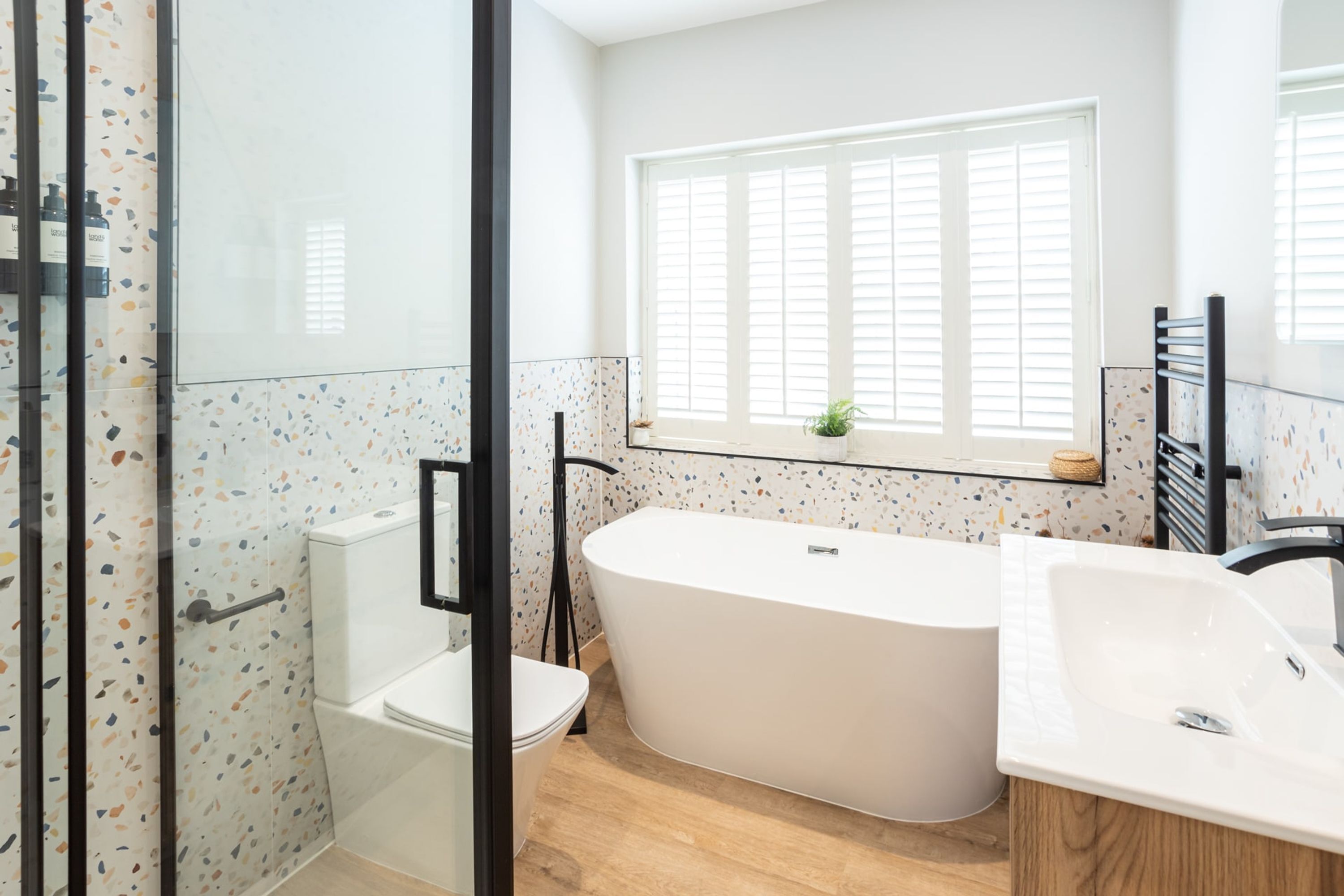 A modern bathroom with a freestanding bathtub, a glass shower enclosure, and a window with blinds.