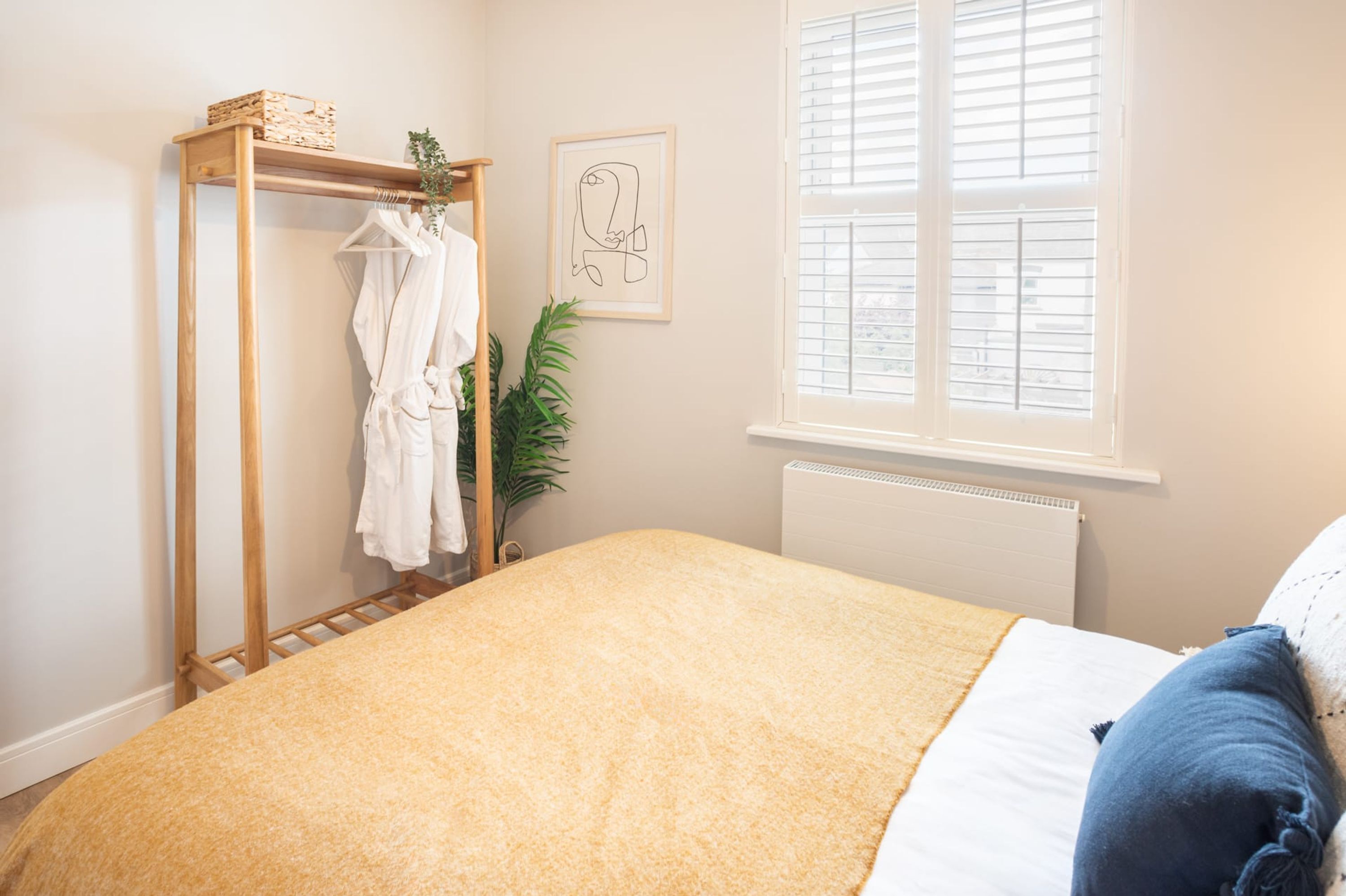 Een slaapkamer met een bed, een houten garderobe, een radiator, een raam en een ingelijste foto aan de muur.