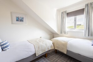 Quarto com duas camas de solteiro, janela com cortinas, radiador e um quadro emoldurado na parede.