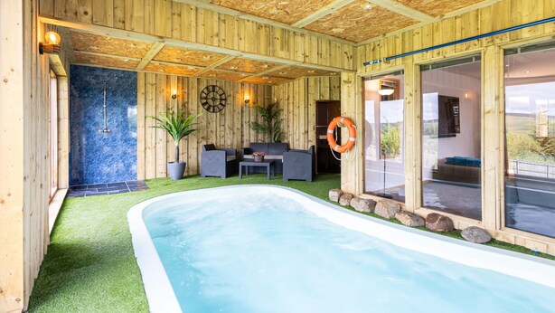 Une cabane en bois dotée d’un bain à remous, d’un coin salon avec une table et des chaises, et d’une grande fenêtre offrant une vue imprenable.