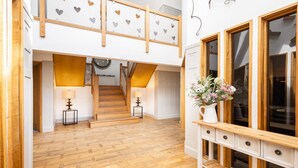 Un loft spacieux avec un escalier en bois, un mur blanc orné de motifs en forme de cœur et une grande fenêtre avec un vase blanc rempli de fleurs.