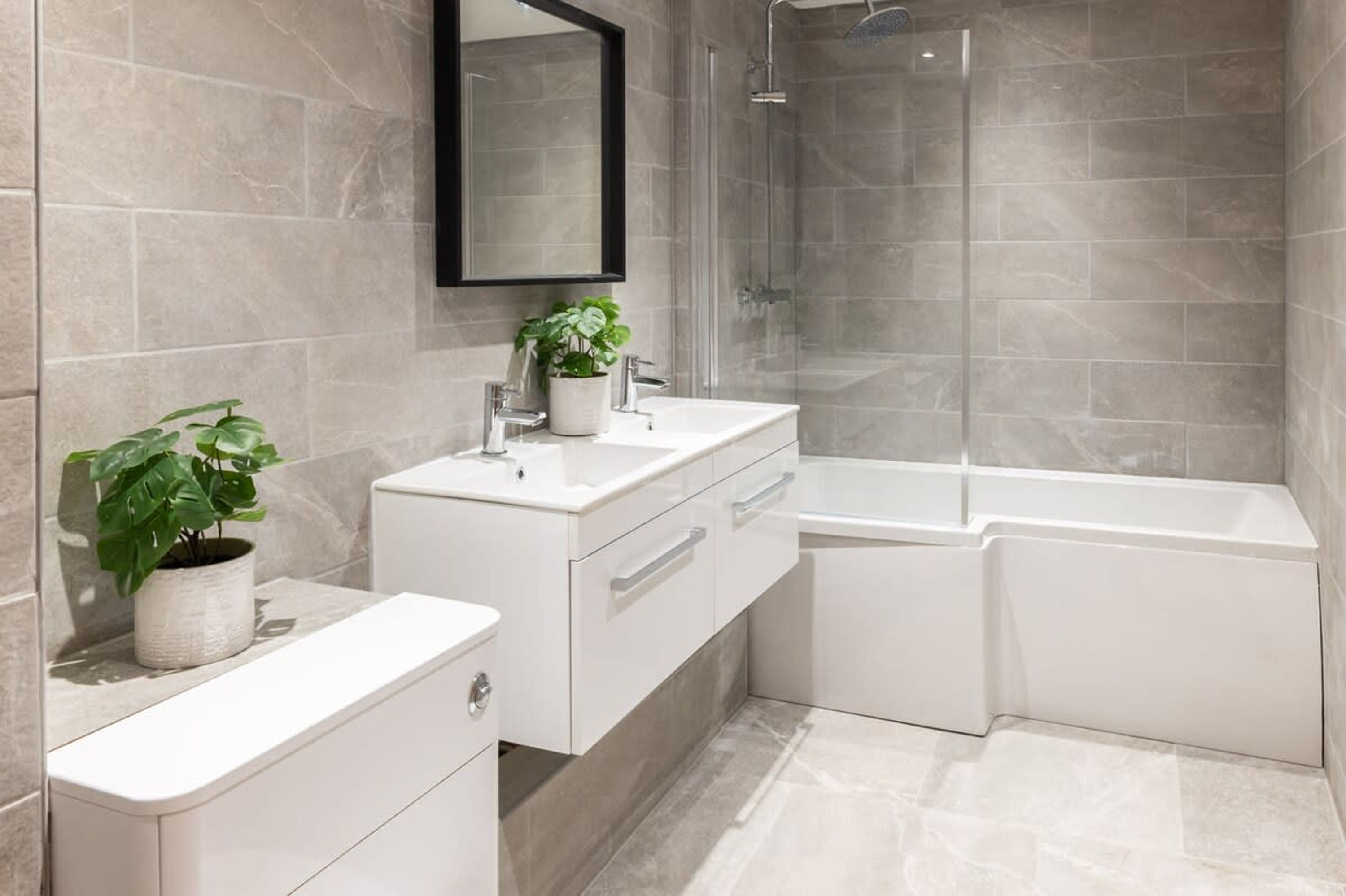Une salle de bain moderne avec un meuble-lavabo blanc, un grand miroir, une plante en pot, une douche et une baignoire.
