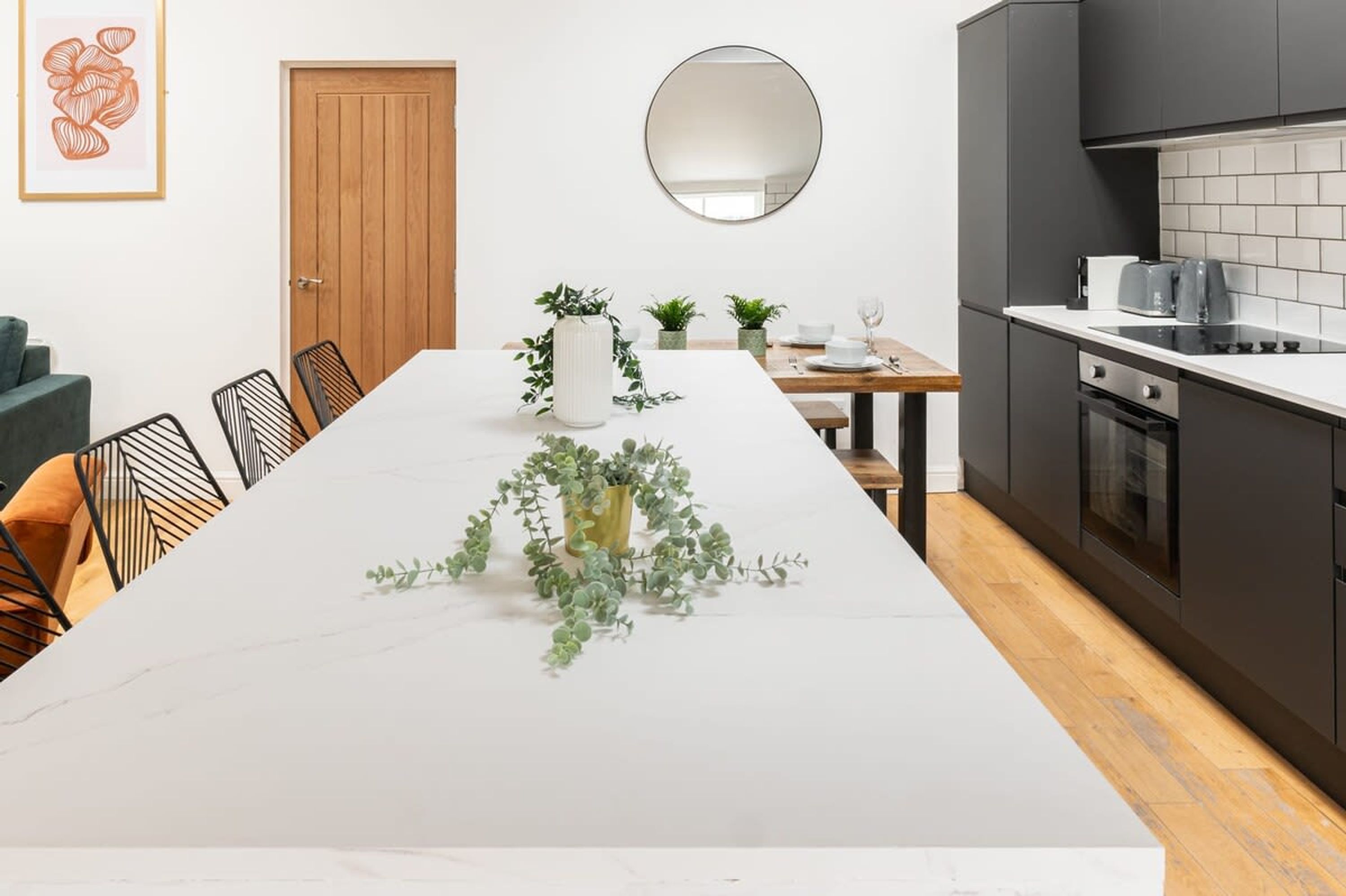 A modern kitchen with dark cabinets, a white countertop, and a wooden dining table with chairs.