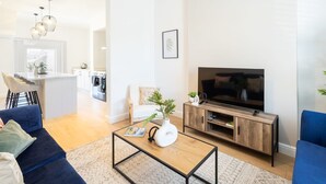 Ein modernes Wohnzimmer mit Sofa, Couchtisch, Fernseher und einer Küche im Hintergrund.