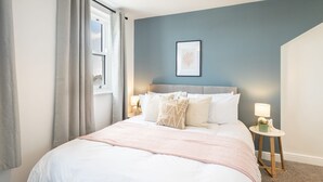 Ein Schlafzimmer mit einem Bett, einem Nachttisch mit Lampe und einem gerahmten Bild an der Wand.