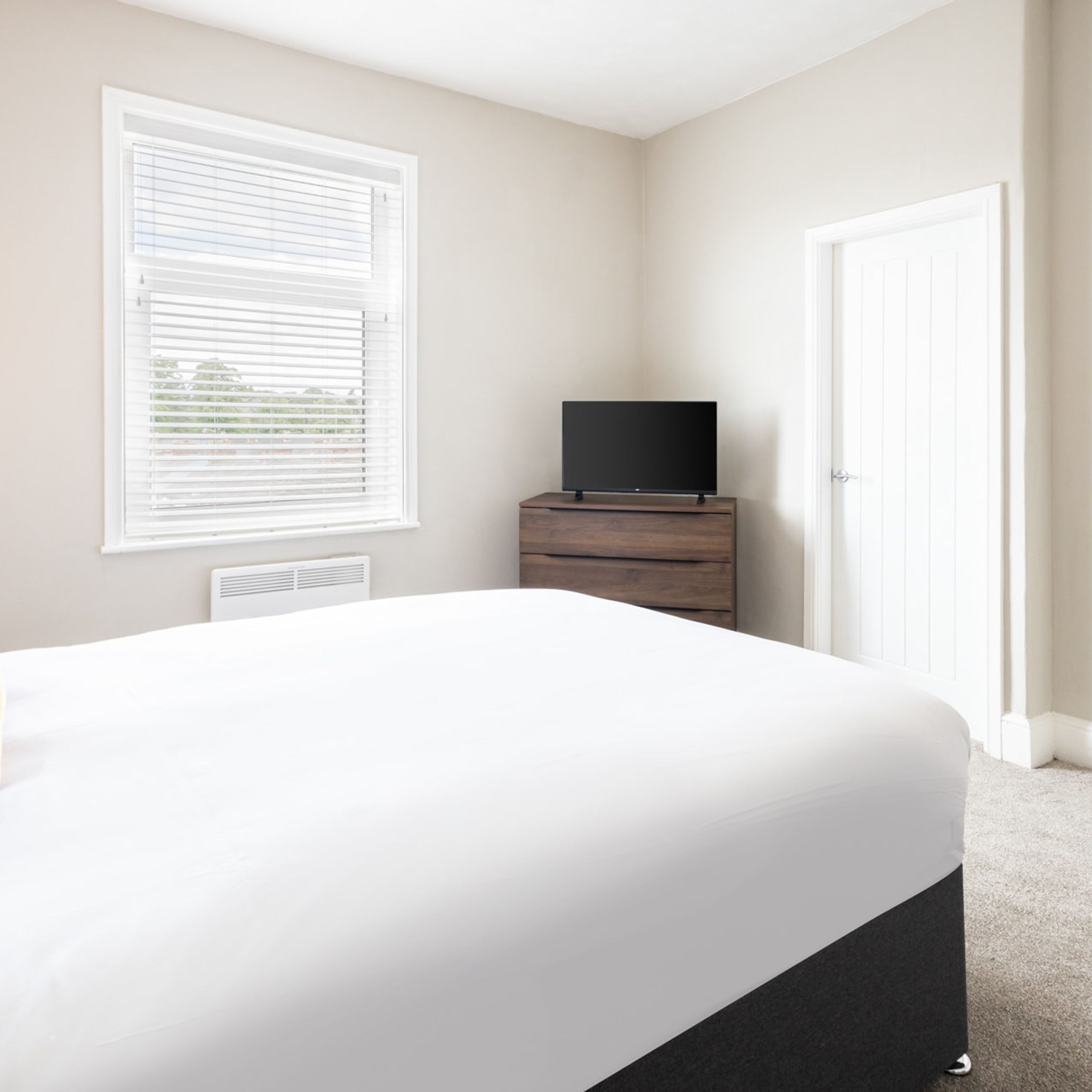 A bedroom with a bed, a dresser, a television on top, and a door.