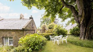 A stone house with a thatched roof, a grassy yard, and white plastic chairs. - Host Stay Upper Lodge (Alnwick)