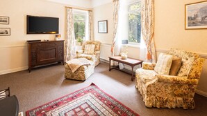 A living room with a flat-screen TV, two floral-patterned armchairs, a wooden cabinet, and a red patterned rug. - Host Stay Upper Lodge (Alnwick)