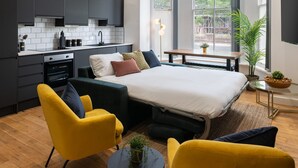 A modern hotel room with a bed, a sofa, a small table, and a kitchen area. - Host Stay Princes Place Hideaway I (Liverpool)
