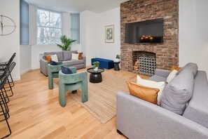 Ein modernes Wohnzimmer mit Kamin aus Backstein, grauen Sofas und einem flachbildfernseher an der Wand.