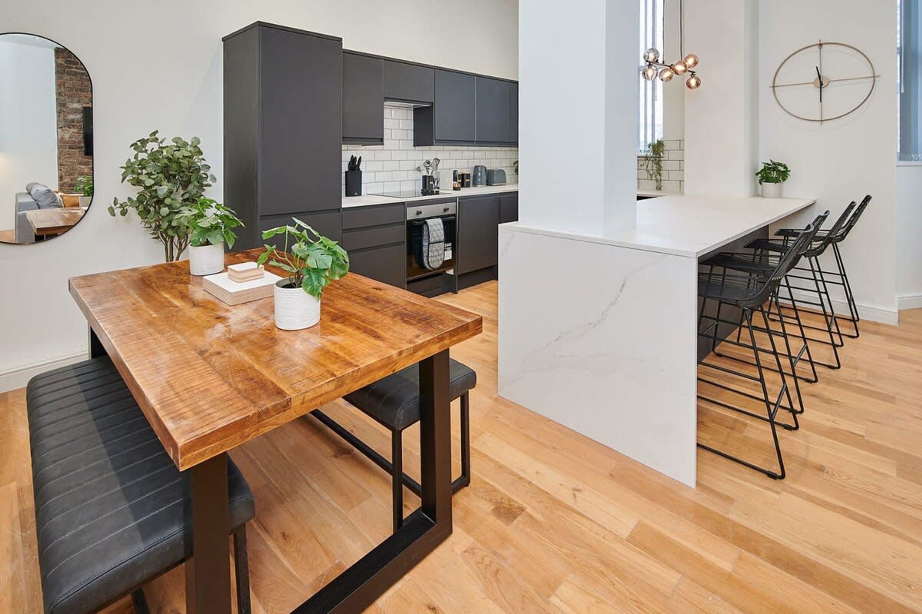 A modern kitchen with dark cabinets, a wooden dining table, and a bar area with black bar stools.