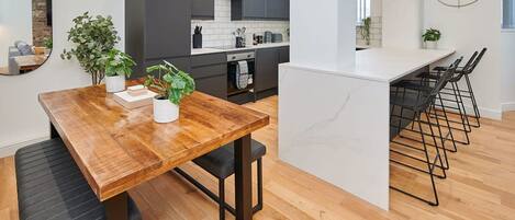 A modern kitchen with dark cabinets, a wooden dining table, and a bar area with black bar stools.